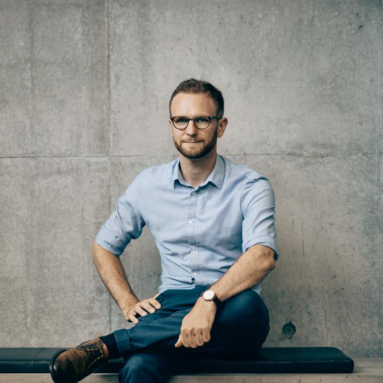 Portrait of Claus Dahl seated on a bench in front of a concrete facade