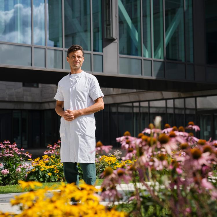 Portræt af Kasper Aaboe omgivet af blomster foran en moderne bygning