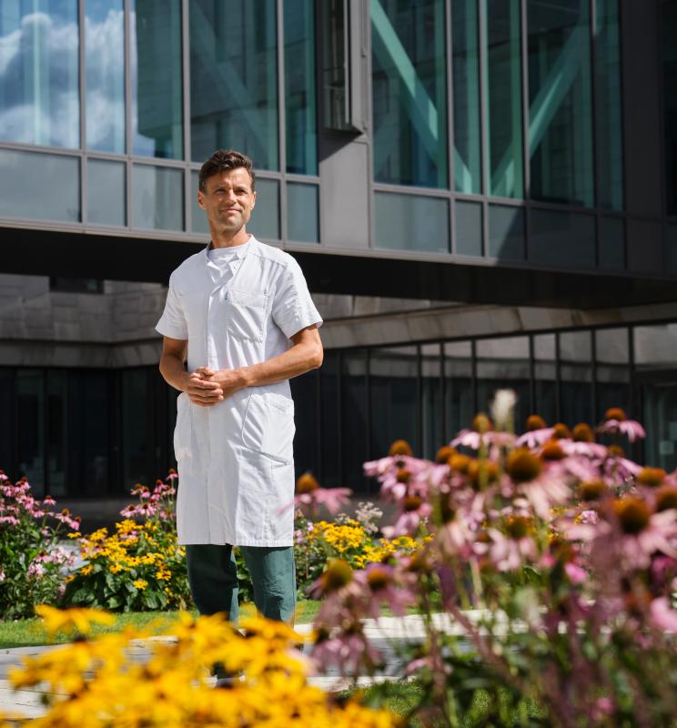 Portræt af Kasper Aaboe omgivet af blomster foran en moderne bygning
