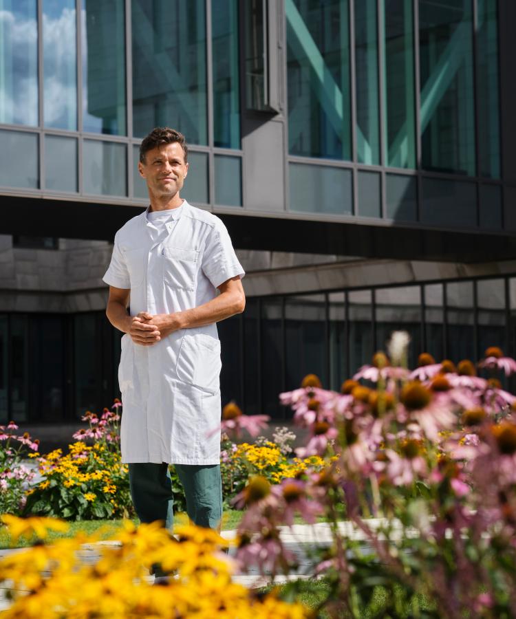 Portrait of Kasper Aaboe surrounded by flowers in front of modern buidling