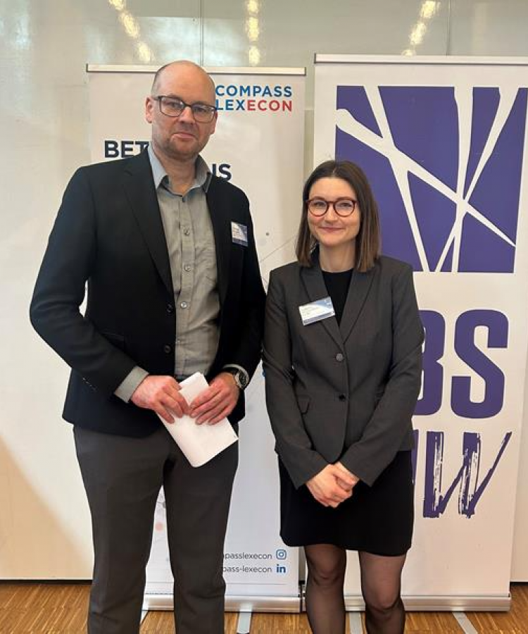 Christian Bergquist and Kathrine Søs Jacobsen Cesko stand in front of two poster at an event hosted by Copenhagen Competition Law Lab