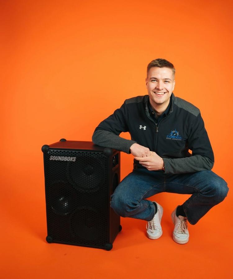 EMBA alumni and co-founder of Soundboks, Christoffer Nyvold posing with a Soundboks in an orange room