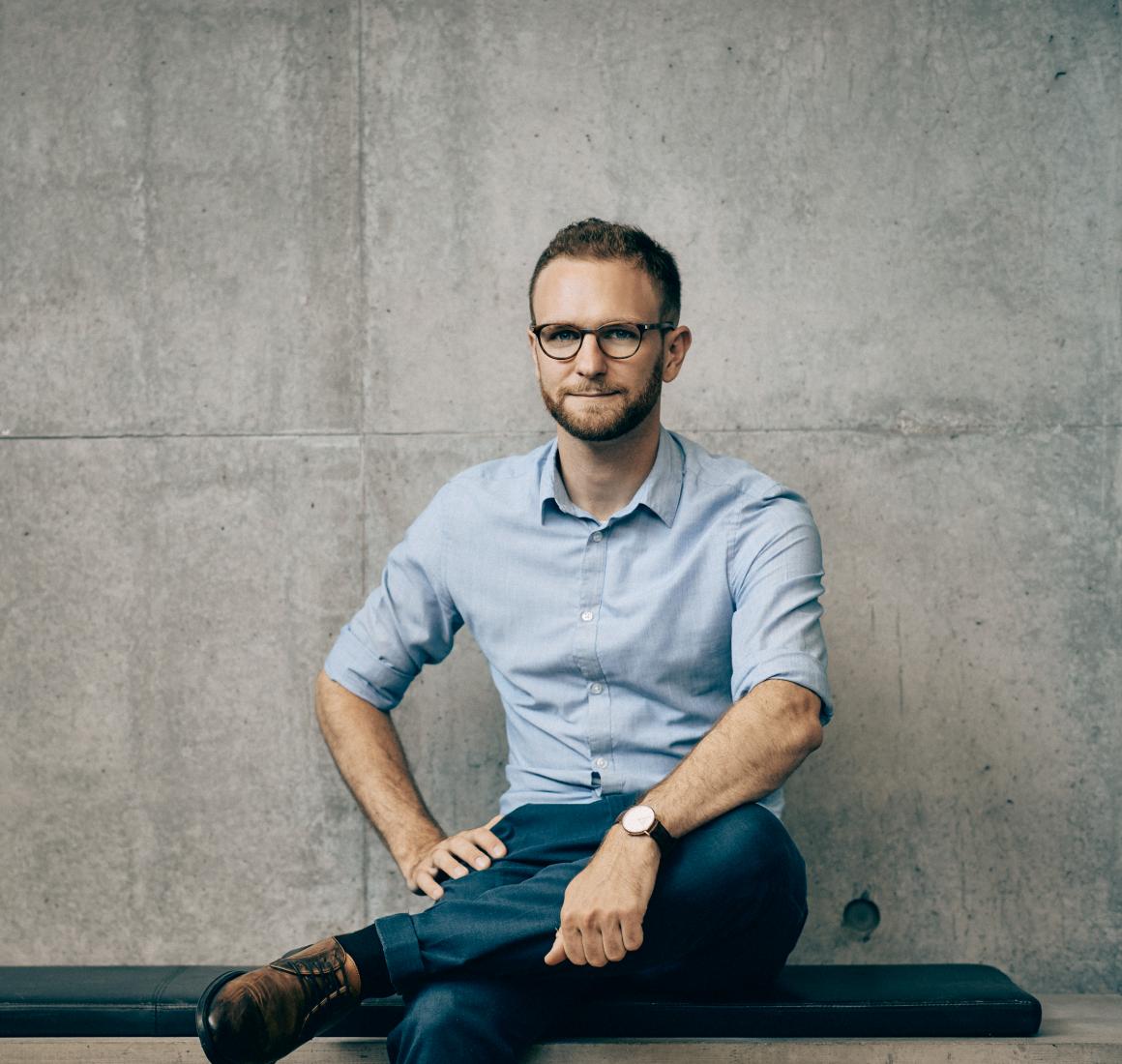 Portrait of Claus Dahl seated on a bench in front of a concrete facade