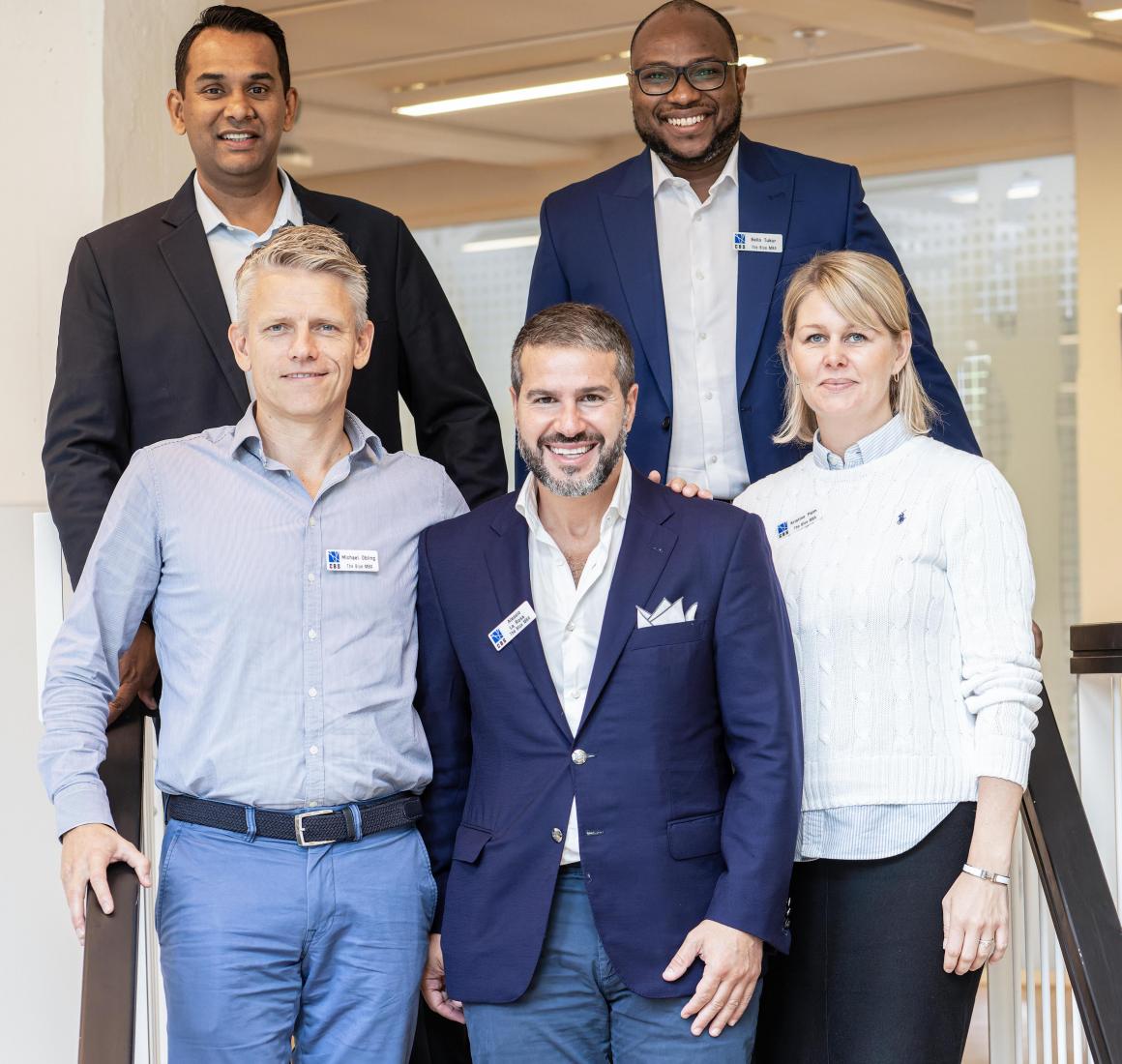 Five Blue MBA participants pose on stairs in front of classroom