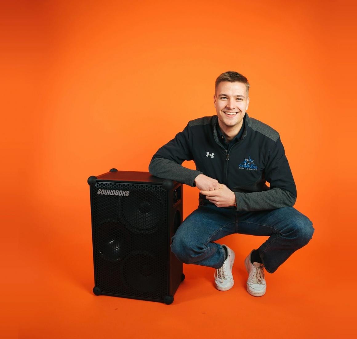 EMBA alumni and co-founder of Soundboks, Christoffer Nyvold posing with a Soundboks in an orange room