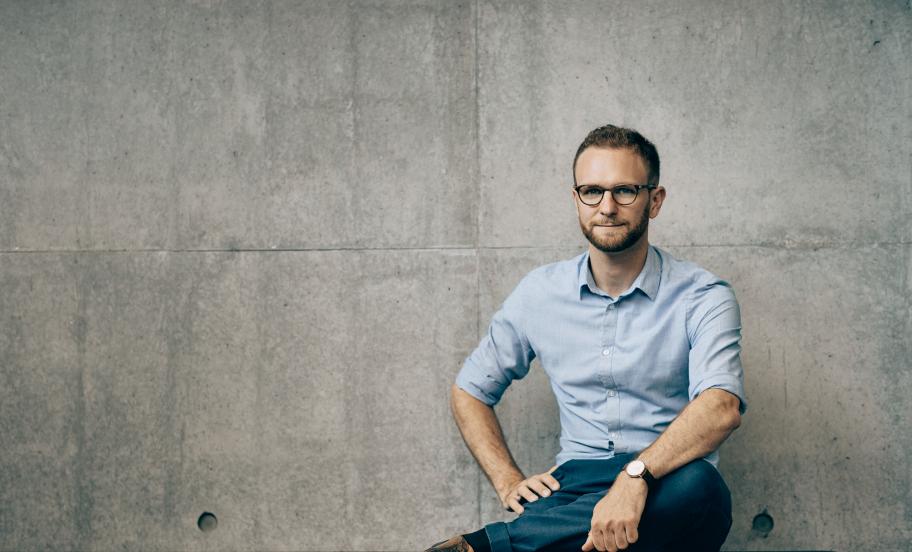 Portræt af Claus Dahl siddende på en bænk foran en betonfacade