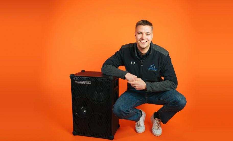 EMBA alumni and co-founder of Soundboks, Christoffer Nyvold posing with a Soundboks in an orange room